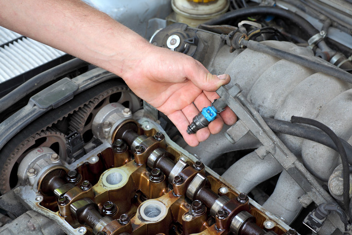 Car mechanic fixing fuel injector at two camshaft gasoline engine